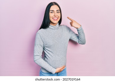 Beautiful Woman With Blue Eyes Expecting A Baby, Touching Pregnant Belly Smiling Cheerful Showing And Pointing With Fingers Teeth And Mouth. Dental Health Concept. 