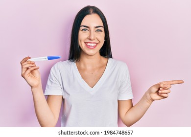 Beautiful woman with blue eyes holding pregnancy test result smiling happy pointing with hand and finger to the side  - Shutterstock ID 1984748657