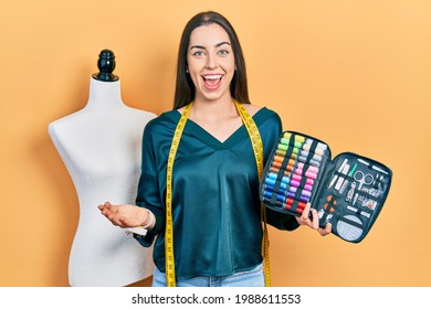 Beautiful woman with blue eyes holding sew kit celebrating achievement with happy smile and winner expression with raised hand 