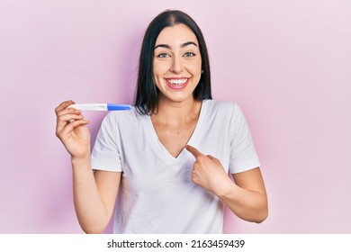 Beautiful woman with blue eyes holding pregnancy test result pointing finger to one self smiling happy and proud  - Shutterstock ID 2163459439