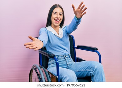 Beautiful woman with blue eyes sitting on wheelchair looking at the camera smiling with open arms for hug. cheerful expression embracing happiness.  - Powered by Shutterstock