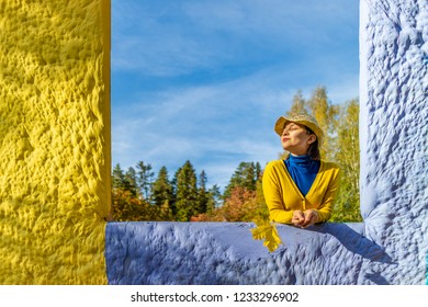 Beautiful Woman In Blue Polo Neck And Yellow Cardigan And A Hat Is Holding Yellow Maple Leaf In Autumn Park