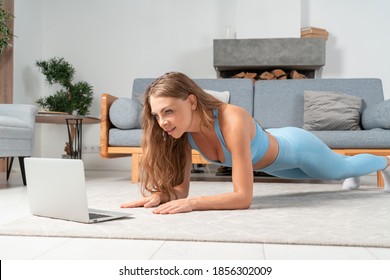 Beautiful Woman In Blue Sportswear Working Her Core Muscles By Plank Exercise At Home Online With Laptop.