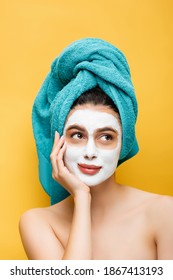 beautiful woman with blue towel on hair and clay mask on face isolated on yellow