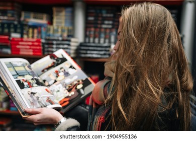 A beautiful woman in a book store holds an open comic book in the ruffs (the book is blurred).