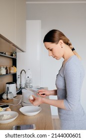 Beautiful Woman Break Chicken Eggs In A Plate In The Kitchen. Cooking Dough.