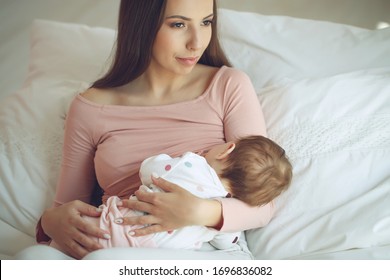 Beautiful woman breastfeeding her baby in a cozy house on the bed.