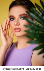 Beautiful Woman With Bright Makeup On A Yellow Background In A Purple Sportswear With A Palm Leaf. Girl On Vacation. Photo In The Style Of The 80s