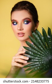 Beautiful Woman With Bright Makeup On A Yellow Background In A Purple Sportswear With A Palm Leaf. Girl On Vacation. Photo In The Style Of The 80s