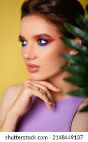 Beautiful Woman With Bright Makeup On A Yellow Background In A Purple Sportswear With A Palm Leaf. Girl On Vacation. Photo In The Style Of The 80s