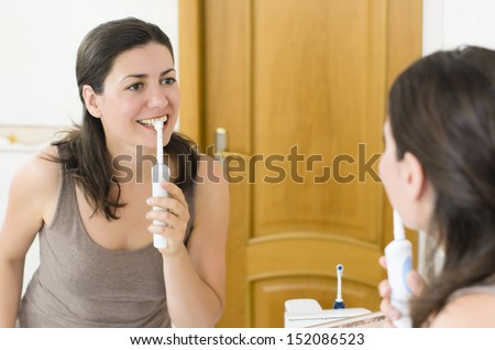 Beautiful woman brushing teeth looking in the mirror