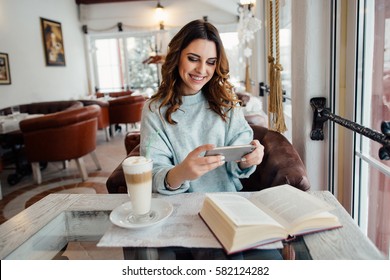 Beautiful woman in cafe watching video on smart phone and smiling 