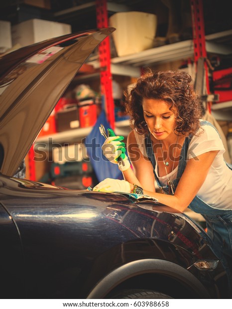 beautiful\
woman car mechanic in a garage, dressed in blue overalls, opened\
the hood of the car and reads the repair manual. Preparing for a\
car trip. Instagram image filter retro\
style