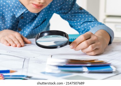 Beautiful woman carefully studying technical drawing with magnifying glass. Designer working with construction blueprint at workplace. Thorough analysis and inspection of design project at desk.