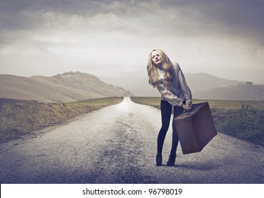 Beautiful woman carrying a suitcase with some difficulty on a countryside road