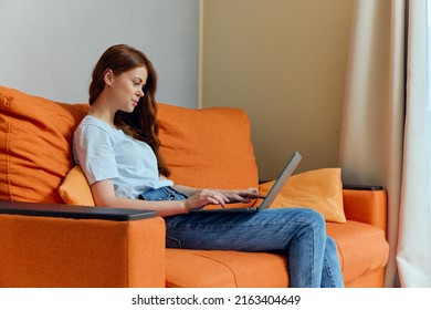 Beautiful Woman Chatting On The Orange Couch With A Laptop Lifestyle