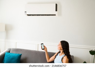 Beautiful Woman Checking The Weather App On Her Smartphone During The Summer While Using The Air Conditioner