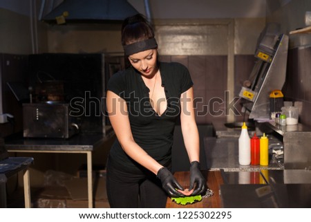beautiful woman chef prepares a hamburger in the kitchen of the restaurant