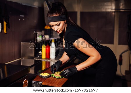 beautiful woman chef prepares a hamburger in the kitchen of the restaurant