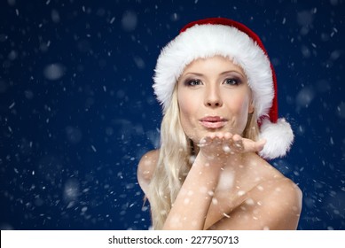 Beautiful woman in Christmas cap blows kiss, winter background - Powered by Shutterstock