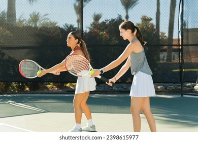 Beautiful woman coach and teen girl taking tennis lessons and practicing their tennis serve on the tennis court - Powered by Shutterstock