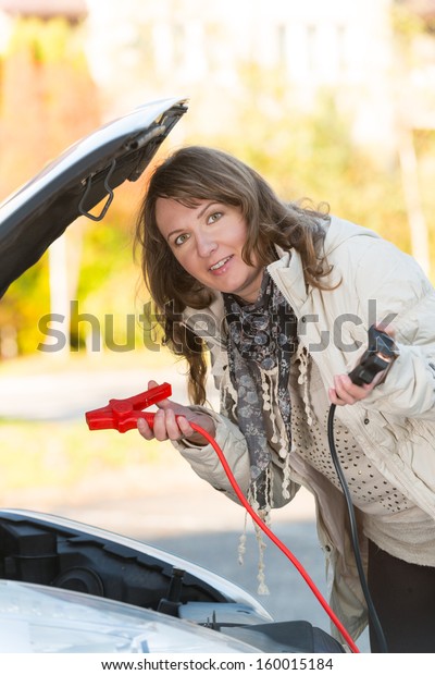 Beautiful woman connecting booster cables to a\
car battery