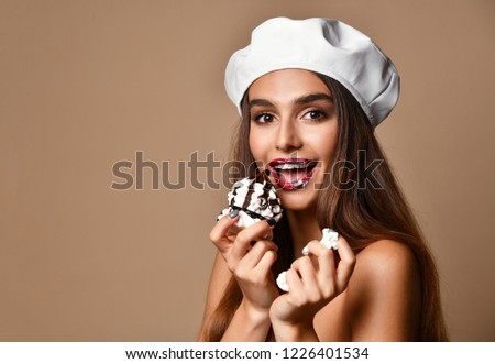 Beautiful woman cook in white cap eat sweet chocolate cake celebrating on light brown background