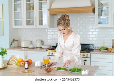 Beautiful woman cooking organic vegetarian salad, slicing strawberries and cheese in home kitchen interior. Girl with Vegan Food fresh ingredients, healthy cooking. In light dress with makeup and hair