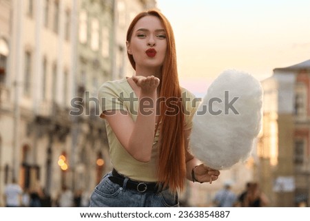 Beautiful woman with cotton candy blowing kiss on city street
