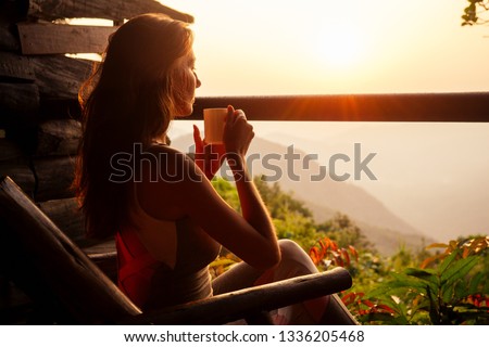 Beautiful woman with cup of coffee tea enjoying the view from the balcony on tea plantation jungle at India Kerala Goa wildernest nature spa resort