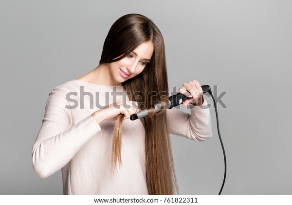 Beautiful\
woman curling long hair using curling iron.\
