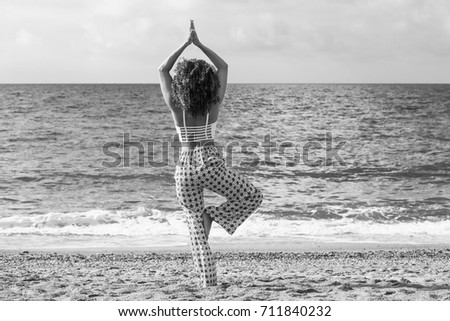 Beautiful woman with curly hair doing yoga on the beach, black and white