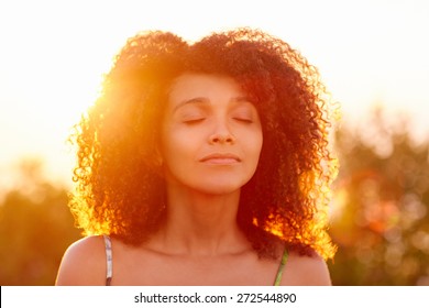 Beautiful Woman With Curly Hair Looking Relaxed And Happy With Her Eyes Closed Against A Golden Sunset With Sun Flare 