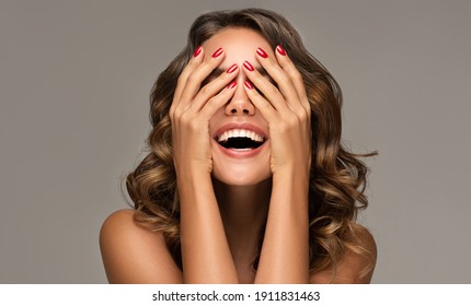 Beautiful woman with curly hair and red nails manicure . Girl happy  laughs  closes her face with a hand .