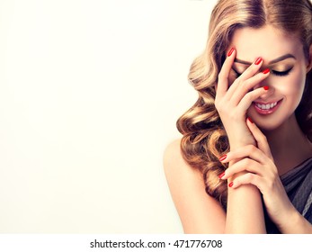 Beautiful Woman With Curly Hair And Red Nails Manicure . Girl Laughs Shyly Closes Her Face With A Hand .