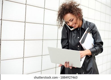 Beautiful Woman With Curly Hair Talking On The Phone And Carrying An Open Laptop