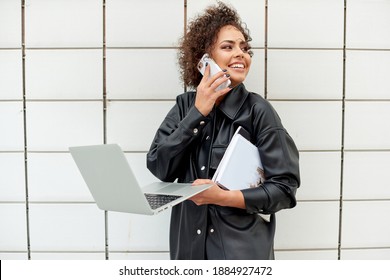 Beautiful Woman With Curly Hair Talking On The Phone And Carrying An Open Laptop