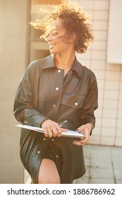 Beautiful Woman With Curly Hair Talking On The Phone And Carrying An Open Laptop