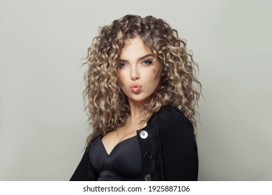 Beautiful woman with curly hairstyle blowing kiss on white background