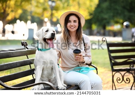 Beautiful woman with cute Labrador sitting on bench in park