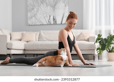 Beautiful woman with cute red cat practicing yoga on mat at home - Powered by Shutterstock