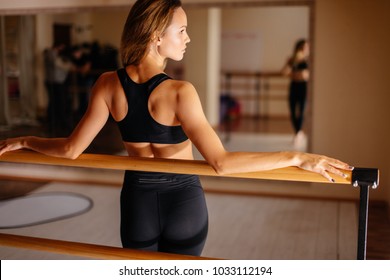 Beautiful woman dancer posing near barre in ballet studio.
