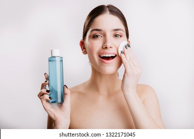 Beautiful woman delicately moisturizes skin with cosmetic tonic. Portrait of lady with healthy skin without makeup on isolated background