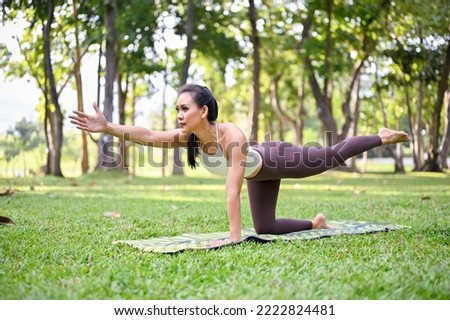 Beautiful woman doing bird dog yoga pose and stretching her body at the park in the morning,  healthy lifestyle and activity concept
