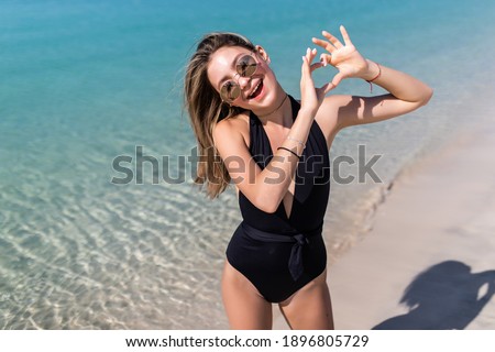 Beautiful woman doing selfie with heart gesture on the beach