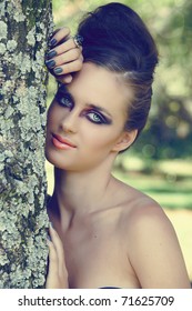 Beautiful Woman With Dramatic Eye Make-up, Gray Manicure & Beehive Hairstyle Outdoors Next To The Tree With Natural Bokeh Effect, Split Tone Colour For Fashion Look.