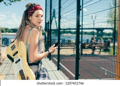 Beautiful woman with dreadlocks looking relaxed and turning her head while being outdoors with modern device and her smartphone - Powered by Shutterstock