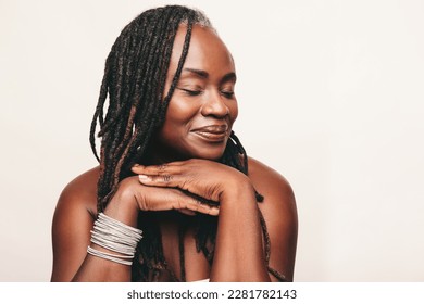 Beautiful woman with dreadlocks smiling with her eyes closed in a studio. Mature woman wearing light make-up against a white background. Happy middle-aged woman pampering her ageing body. - Shutterstock ID 2281782143