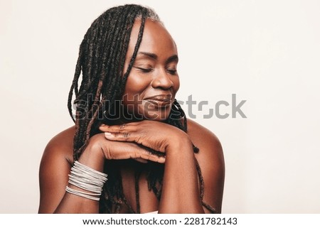 Beautiful woman with dreadlocks smiling with her eyes closed in a studio. Mature woman wearing light make-up against a white background. Happy middle-aged woman pampering her ageing body.