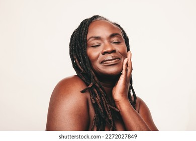 Beautiful woman with dreadlocks touching her flawless skin with her eyes closed. Confident dark-skinned woman embracing her smooth melanated skin. Mature black woman ageing gracefully.